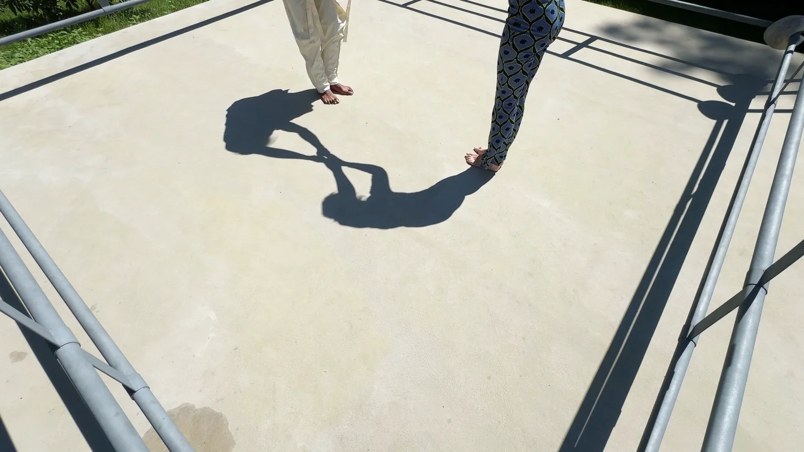 ALOKA · SHADOW — zwei Paar Beine am oberen Bildrand, die Schatten verbinden sich auf der Fläche, Standbild