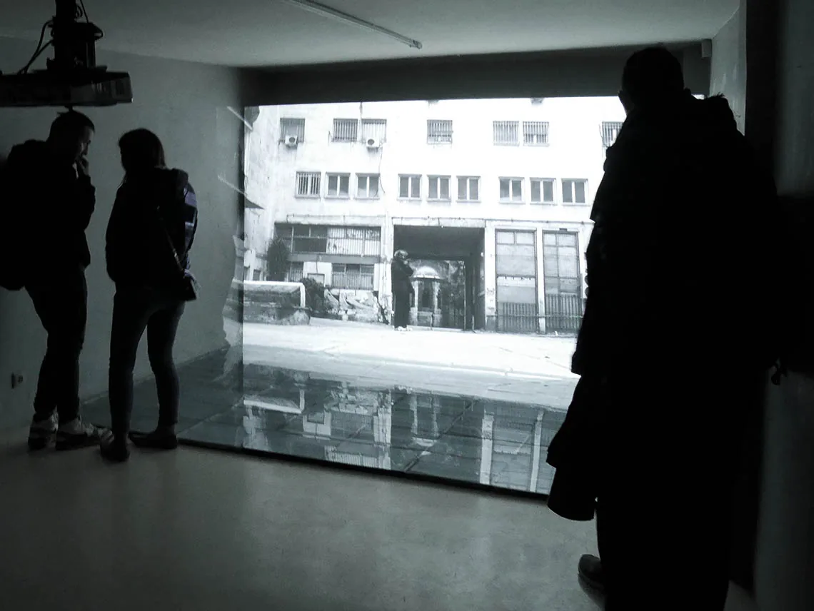 Condensate Mirror — Besucherinnen und Besucher vor der projizierten Videoarbeit „earning from Athens