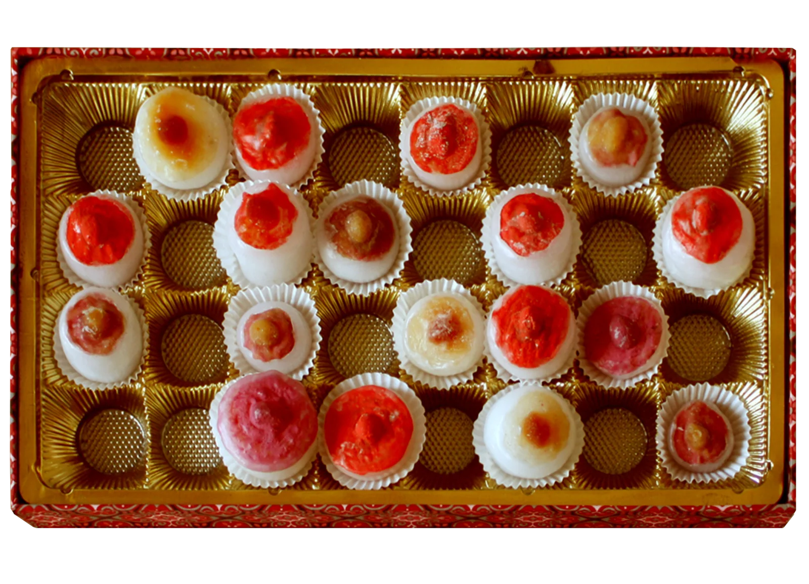 Nahaufnahme einer goldenen Konfektschachtel mit den Pseudo-Pralinen: weiße Wachs- und Latexformen mit roten und rosa Spitzen in weißen Papierförmchen