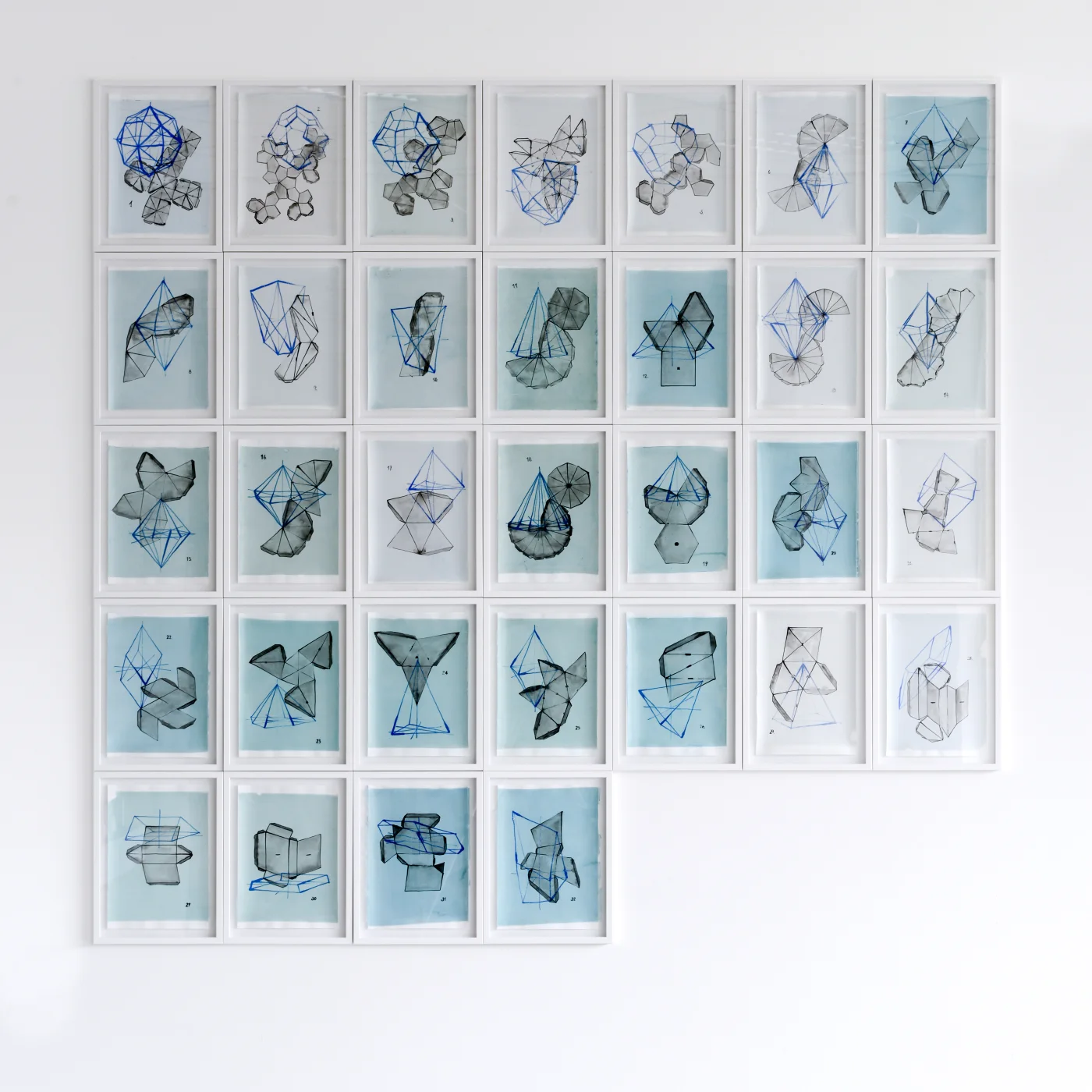 32 Kristallmodelle — die 32 gerahmten Zeichnungen als Wandinstallation: entfaltete Kristallmodelle in Grau, überlagert von bläulich gezeichneten Kristallkörpern, 2015/16
