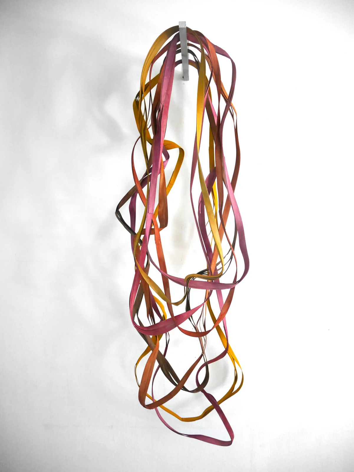 LOOPS — Ellipsenhängung farbig: lange Schlaufen aus roten, gelben und braunen Pappstreifen hängen von der Wand