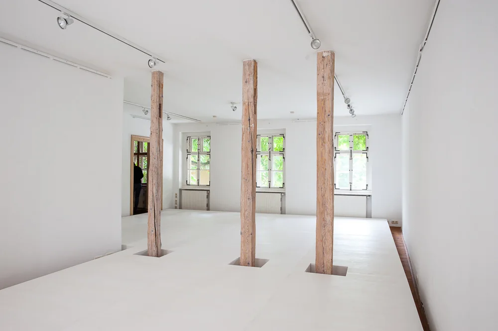 RAUMVERSCHIEBUNG II — der weiße doppelte Boden mit drei Holzstützen, dahinter die Fenster der Galerie