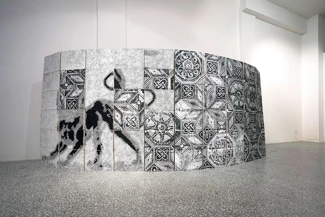 SPOLIA — freistehende, gebogene Mauer aus Faltschachteln, links das hellenistische Löwenmotiv als reliefartiges Punktraster, rechts der römische Mosaikboden als Linolschnitt, 2017