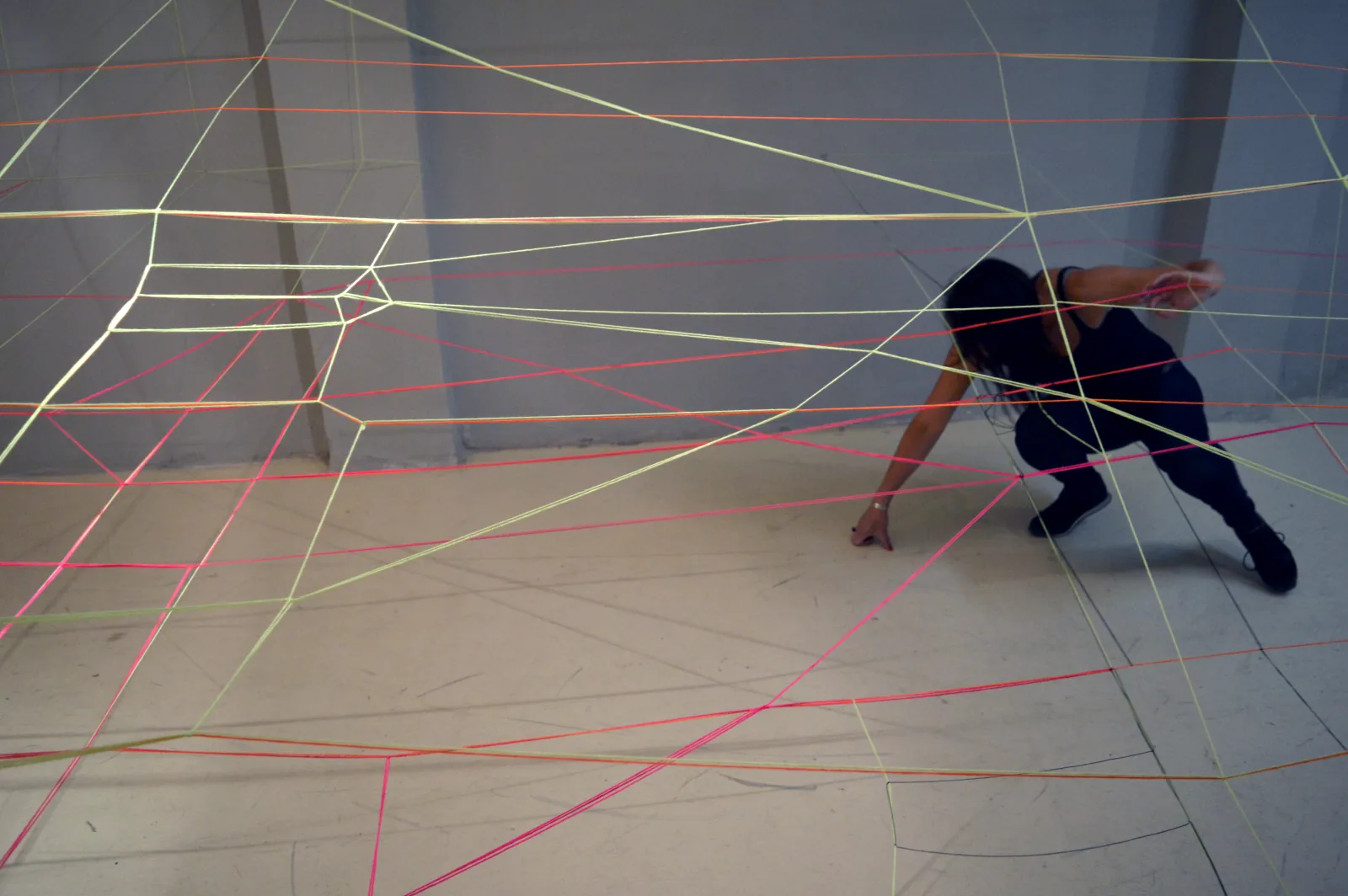 STADTSCHICHTEN — Raumzeichnung aus farbigen, neonleuchtenden Schnüren über zwei schiefen Ebenen im Kellerraum, die Künstlerin im Geflecht, Vlassis Art Gallery Thessaloniki 2016