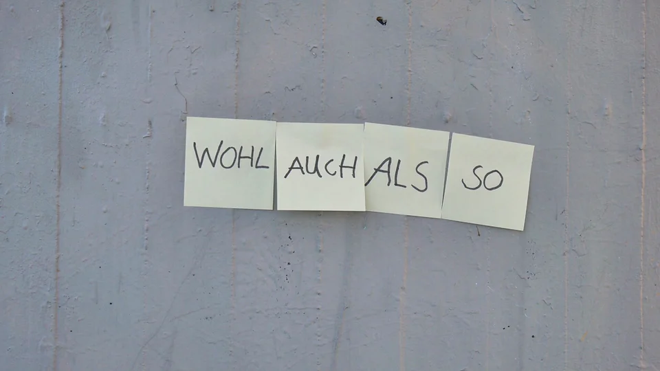 SO AUCH — Zettel mit den Wörtern WOHL, AUCH, ALS und SO an einer Betonwand; startet das Video