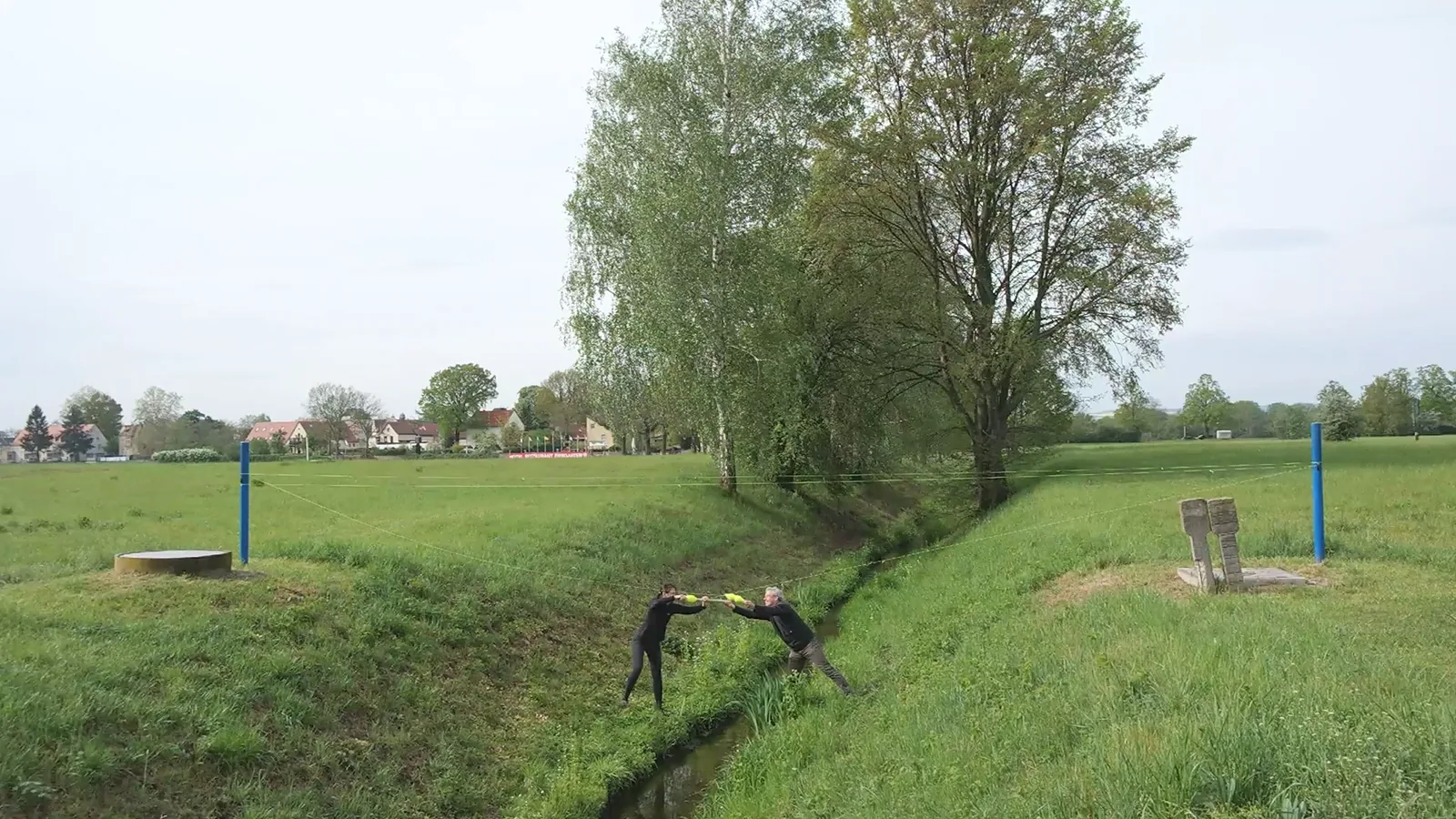 zusammen rumspinnen — die beiden reichen sich über den Bachlauf hinweg den Faden, seitlich gesehen, Standbild
