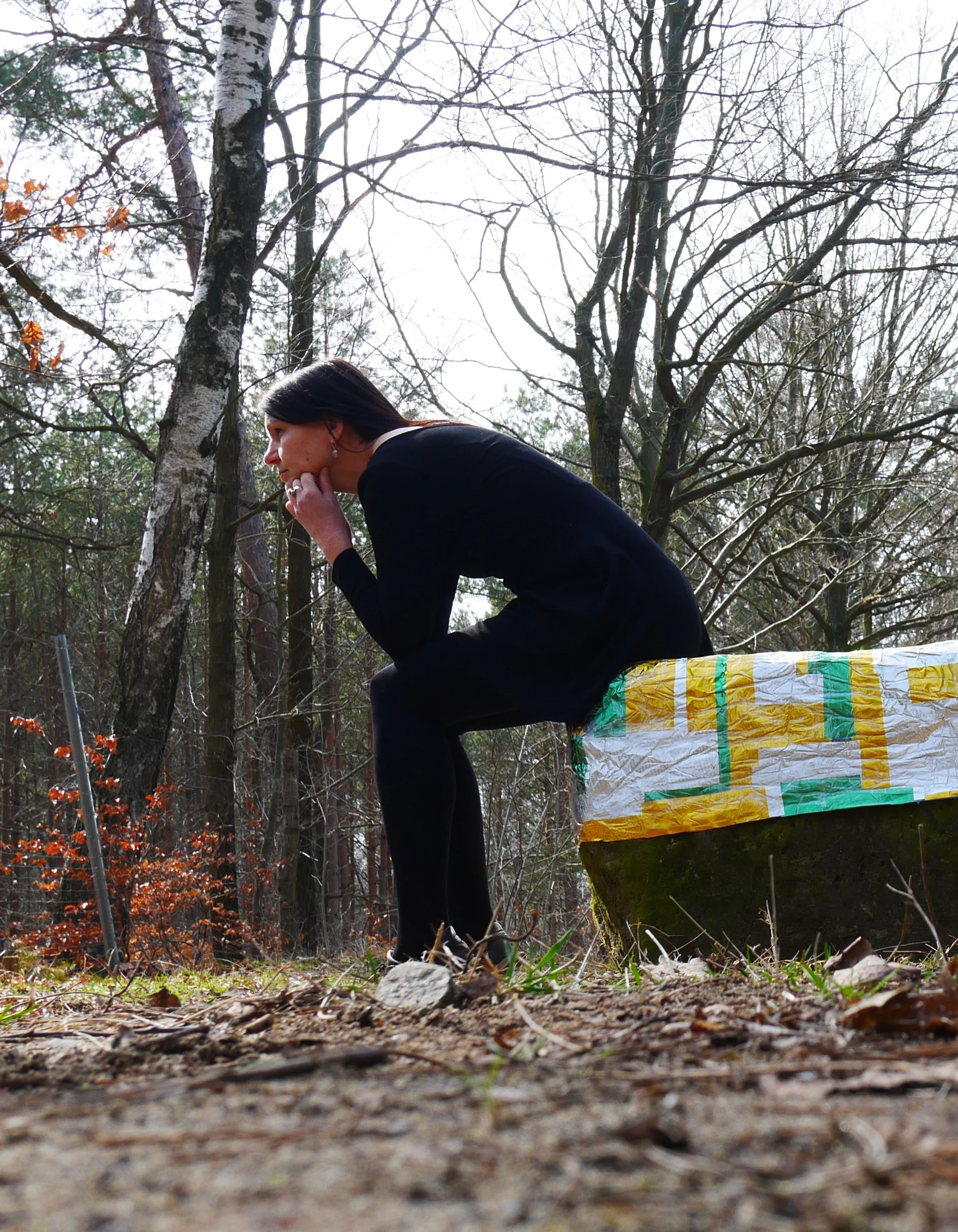 Birgit Schuh beobachtet, sitzend an einem bemalten Kunstobjekt im Wald