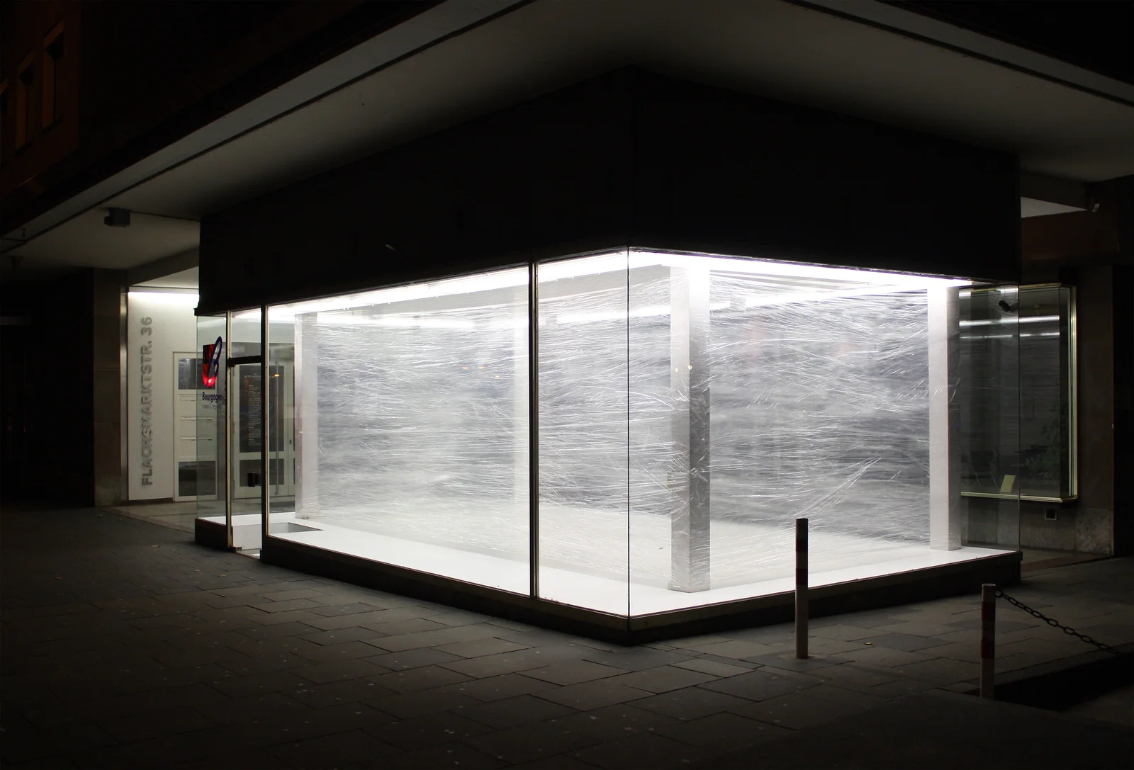 RAUMVERSCHIEBUNG I — der gläserne Pavillon bei Nacht: innen ein hell erleuchteter, mit Folie umspannter Raum zwischen den Stützen